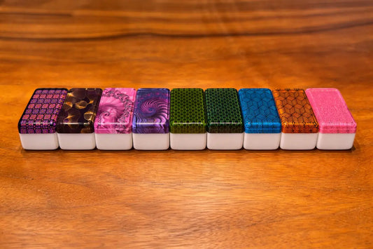 A row of nine mahjong tiles showing various artistic backs including floral, geometric, and fractal designs.