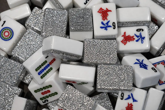 A dense pile of white mahjong tiles with high-intensity silver glitter backs and blue and red engravings.