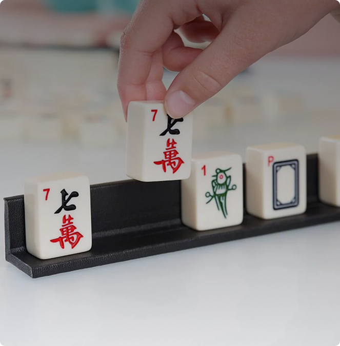Hand placing a white tile with red characters on a Mahjong game setup.