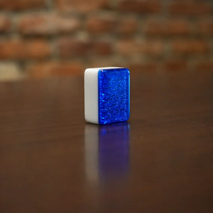 Cube-shaped object with blue glittery surface on a wooden surface with brick wall background