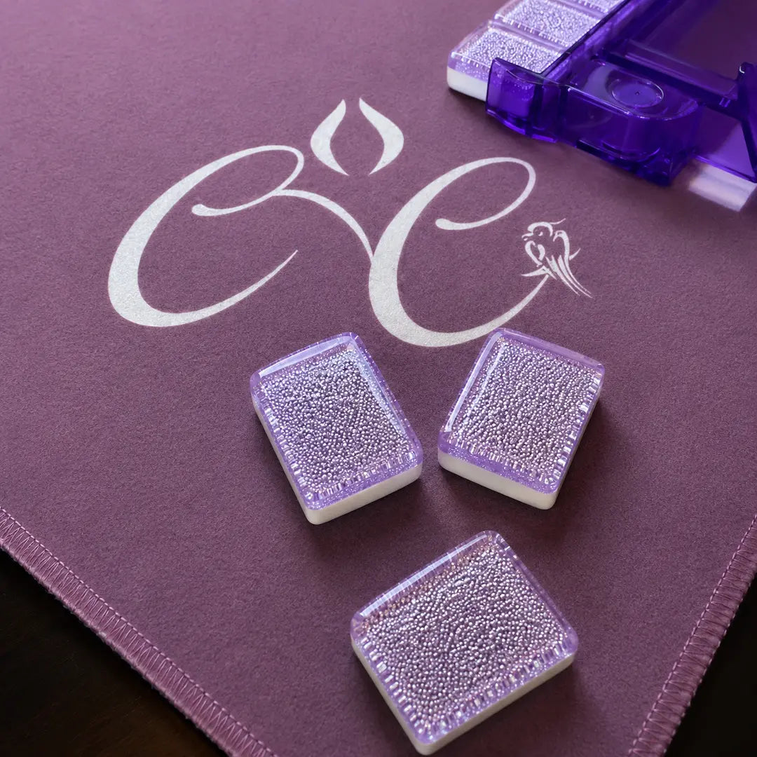 Three purple Mahjong tiles on a purple surface with a logo.