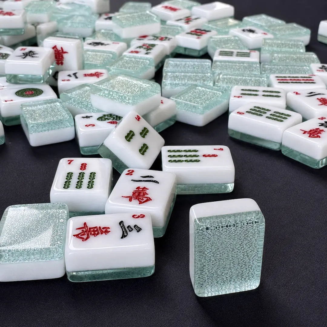 Aqua blue sparkle American Mah Jongg tiles scattered on a dark wooden table