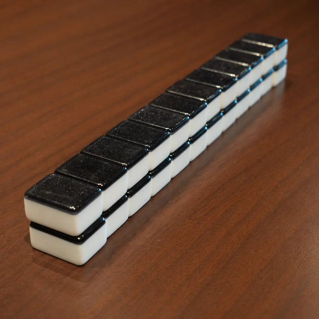 Stacked black automatic Mah Jongg tiles arranged in a row on a wooden table