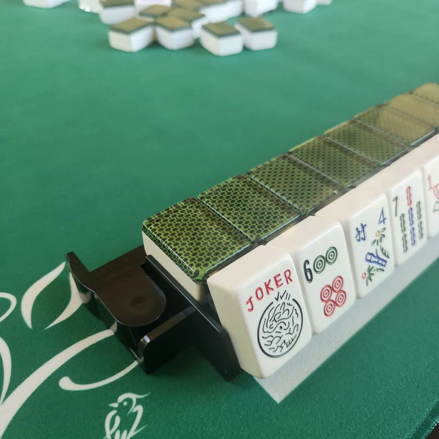 Close-up of a麻将 (mahjong) game with tiles and a holder on a green table.