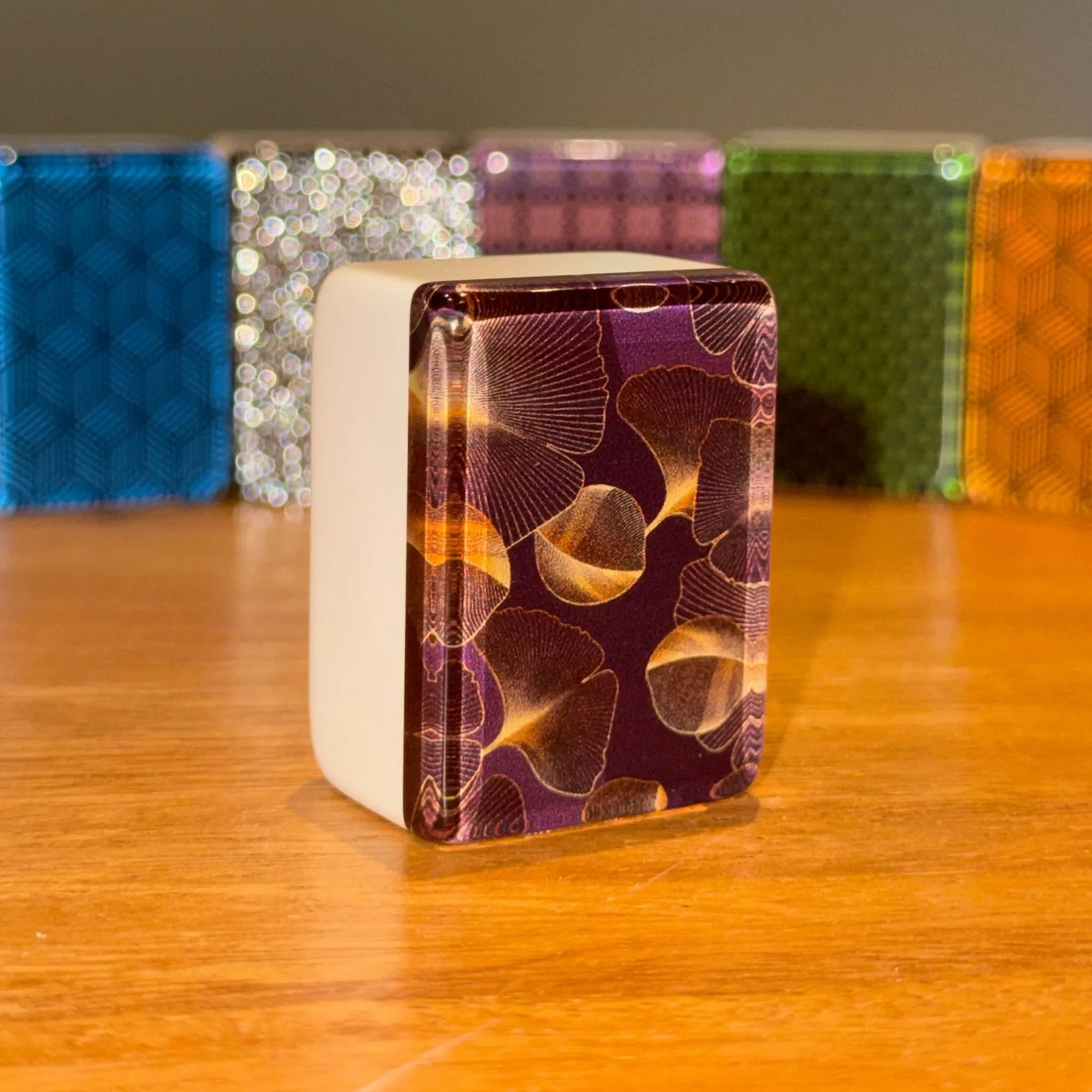 Close up view of a single gingo mah jongg tile standing upright to show the golden ginkgo leaf pattern on a dark background.