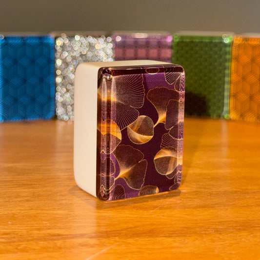 Close up view of a single gingo mah jongg tile standing upright to show the golden ginkgo leaf pattern on a dark background.