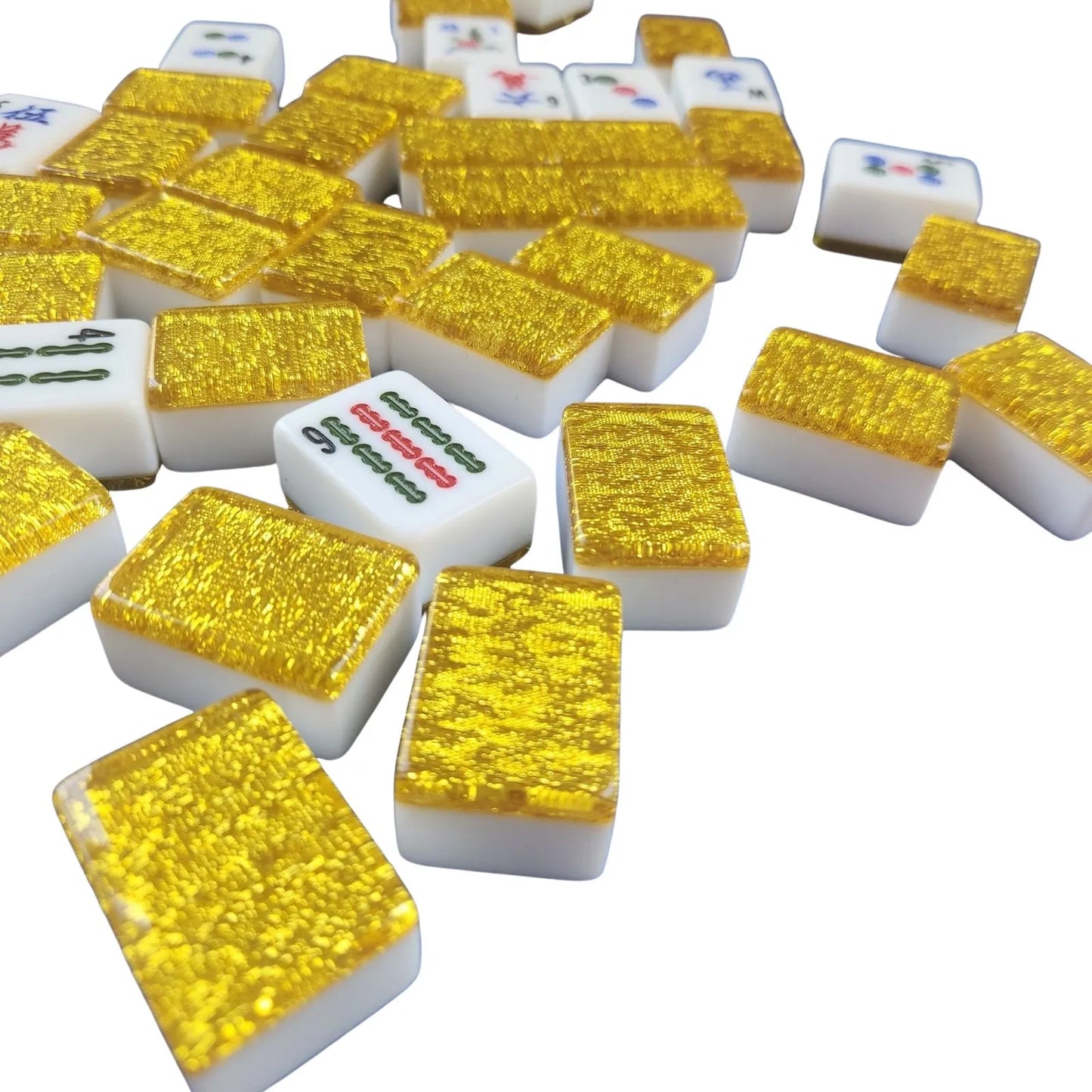 A pile of miniature mahjong tiles with textured gold backs and white fronts showing various Chinese characters, photographed on a clean white background.