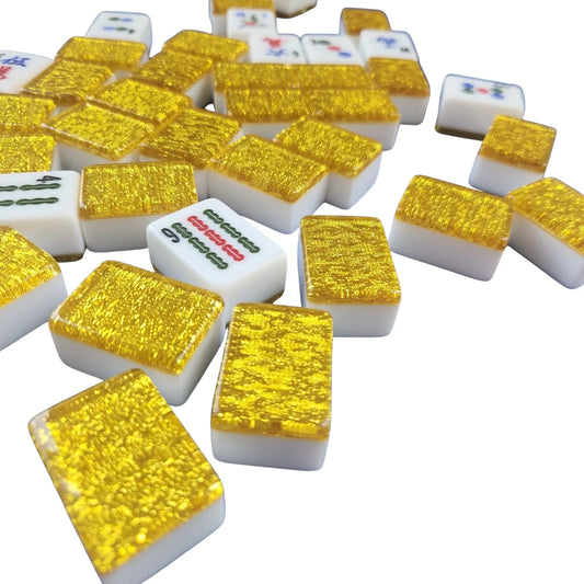 A pile of miniature mahjong tiles with textured gold backs and white fronts showing various Chinese characters, photographed on a clean white background.