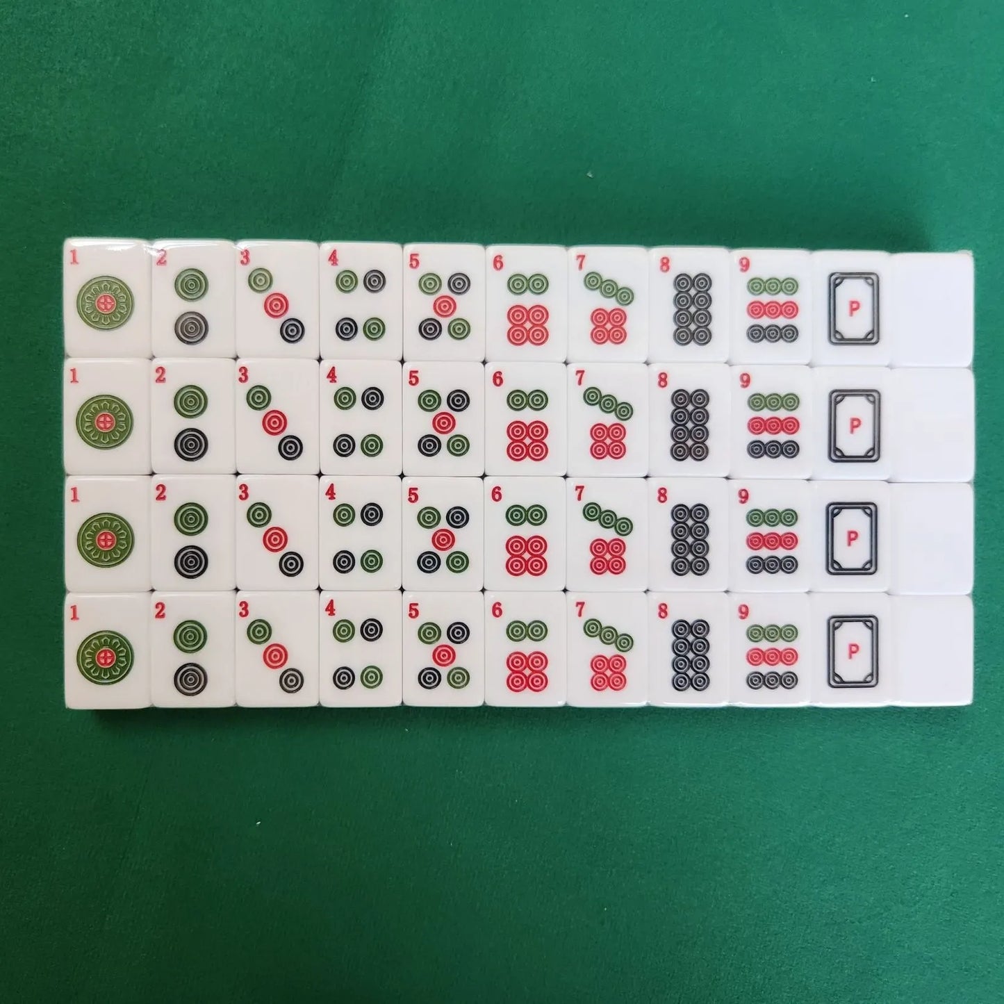 A set of Mahjong tiles arranged in rows on a green felt surface, showing various numbers and symbols in black, red, and green.