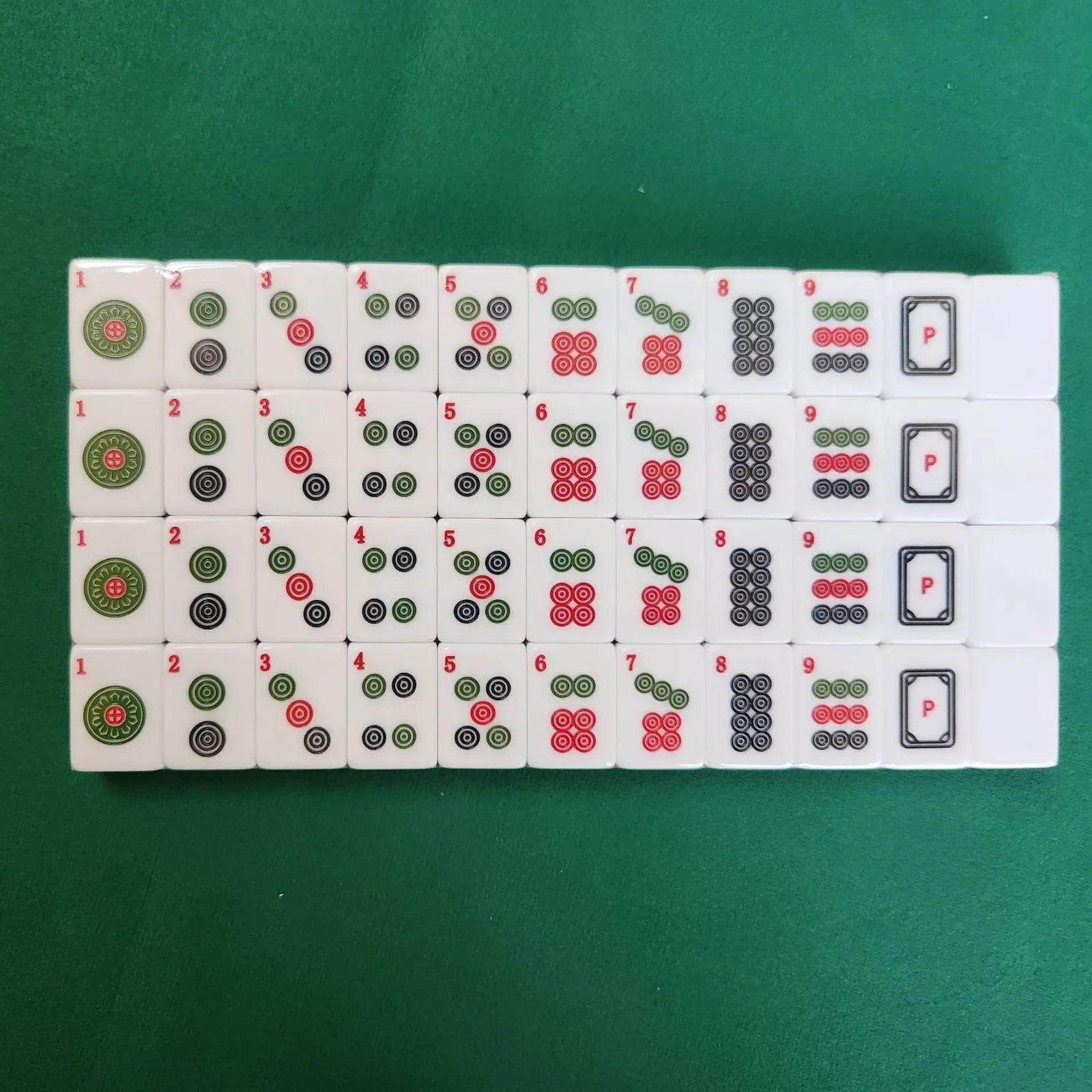 A set of Mahjong tiles arranged in rows on a green felt surface, showing various numbers and symbols in black, red, and green.