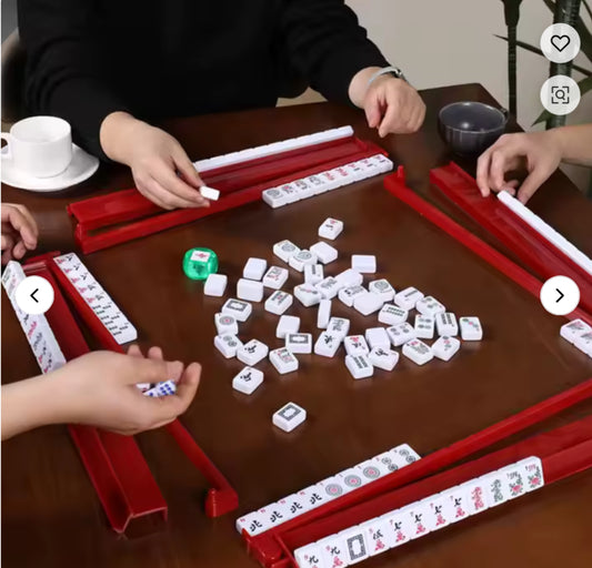 People playing Mahjong with tiles and red racks on a wooden table.