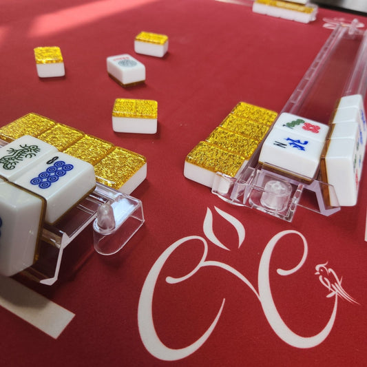 Mahjong tiles on a red table with a brand logo.