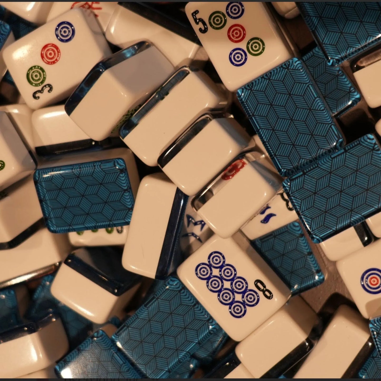 Mixed pile of automatic mah jongg tiles in blue deco weave showing both the engraved faces and geometric back patterns.