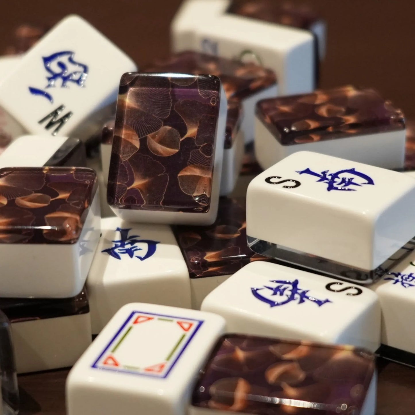 Mixed pile of automatic mah jongg tiles in gingo design showing white engraved faces and gold leaf patterned backs.