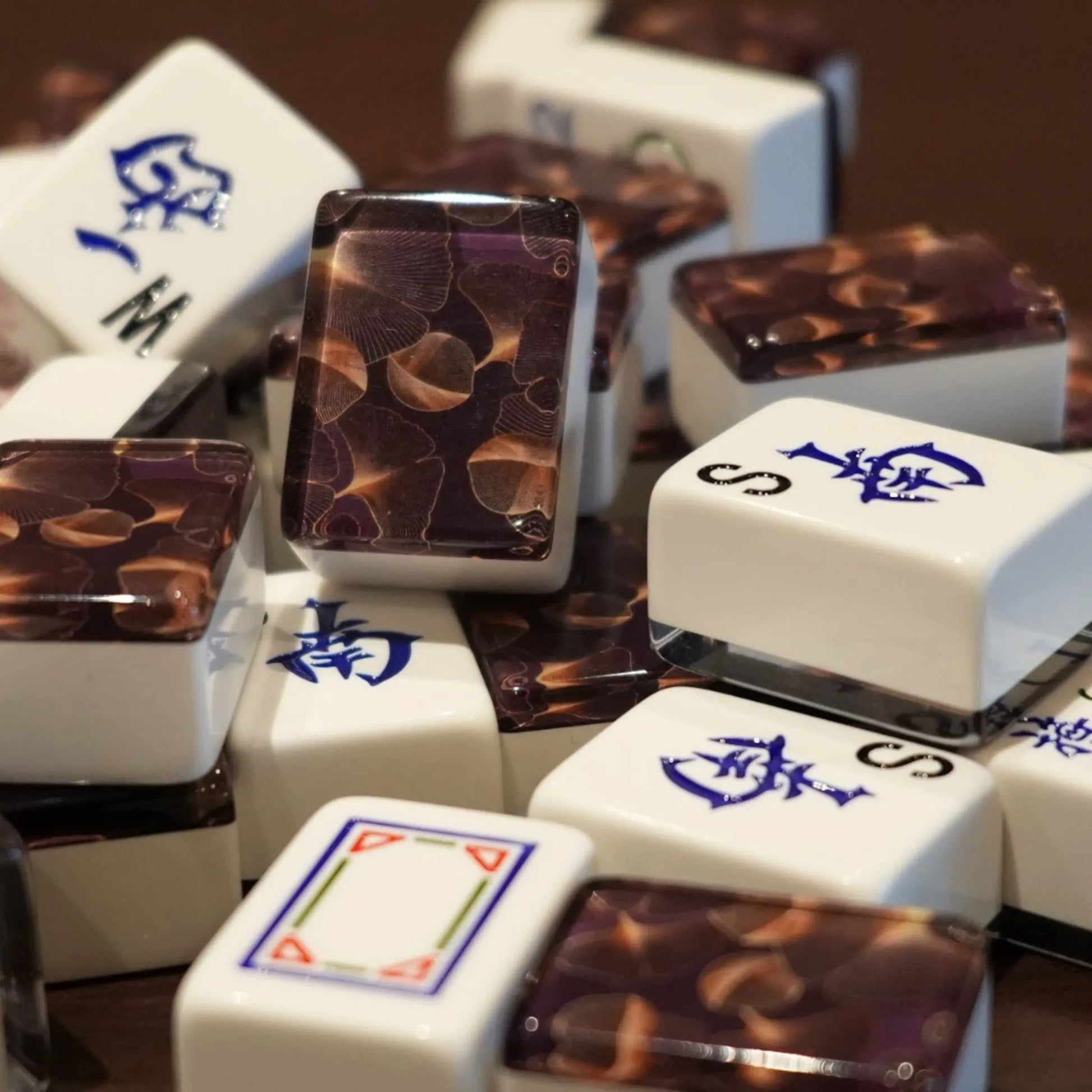 Mixed pile of automatic mah jongg tiles in gingo design showing white engraved faces and gold leaf patterned backs.