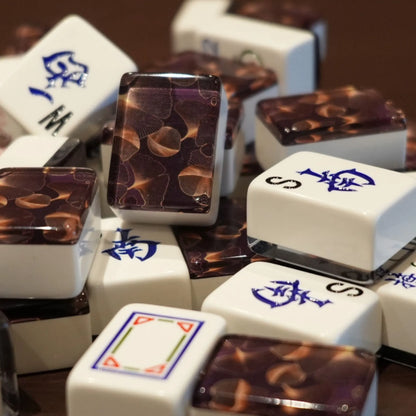 Mixed pile of automatic mah jongg tiles in gingo design showing white engraved faces and gold leaf patterned backs.