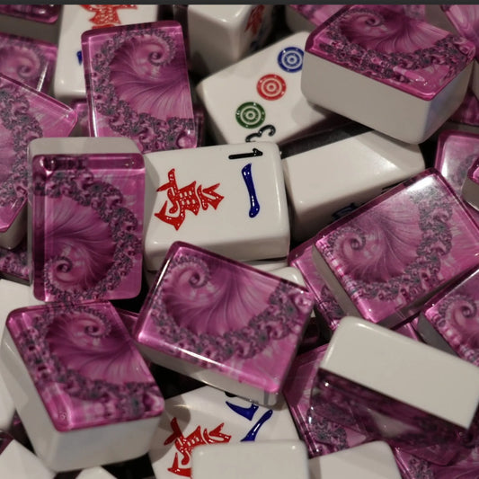 Mixed pile of automatic mah jongg tiles in pink swirl design showing white engraved faces and pink spiral backs.