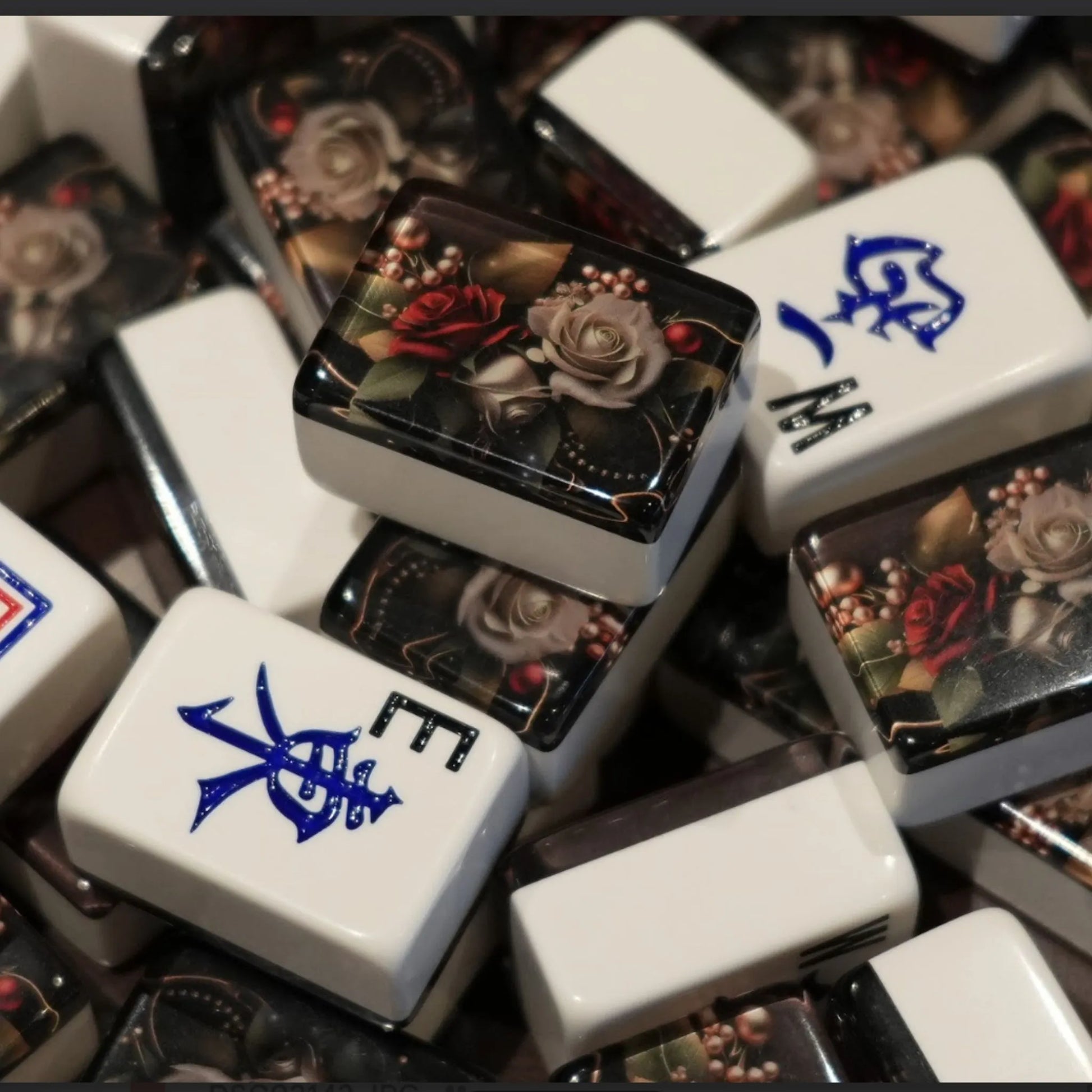 Mixed pile of 36mm automatic mah jongg tiles in rose floral design showing white engraved faces and dark floral backs.