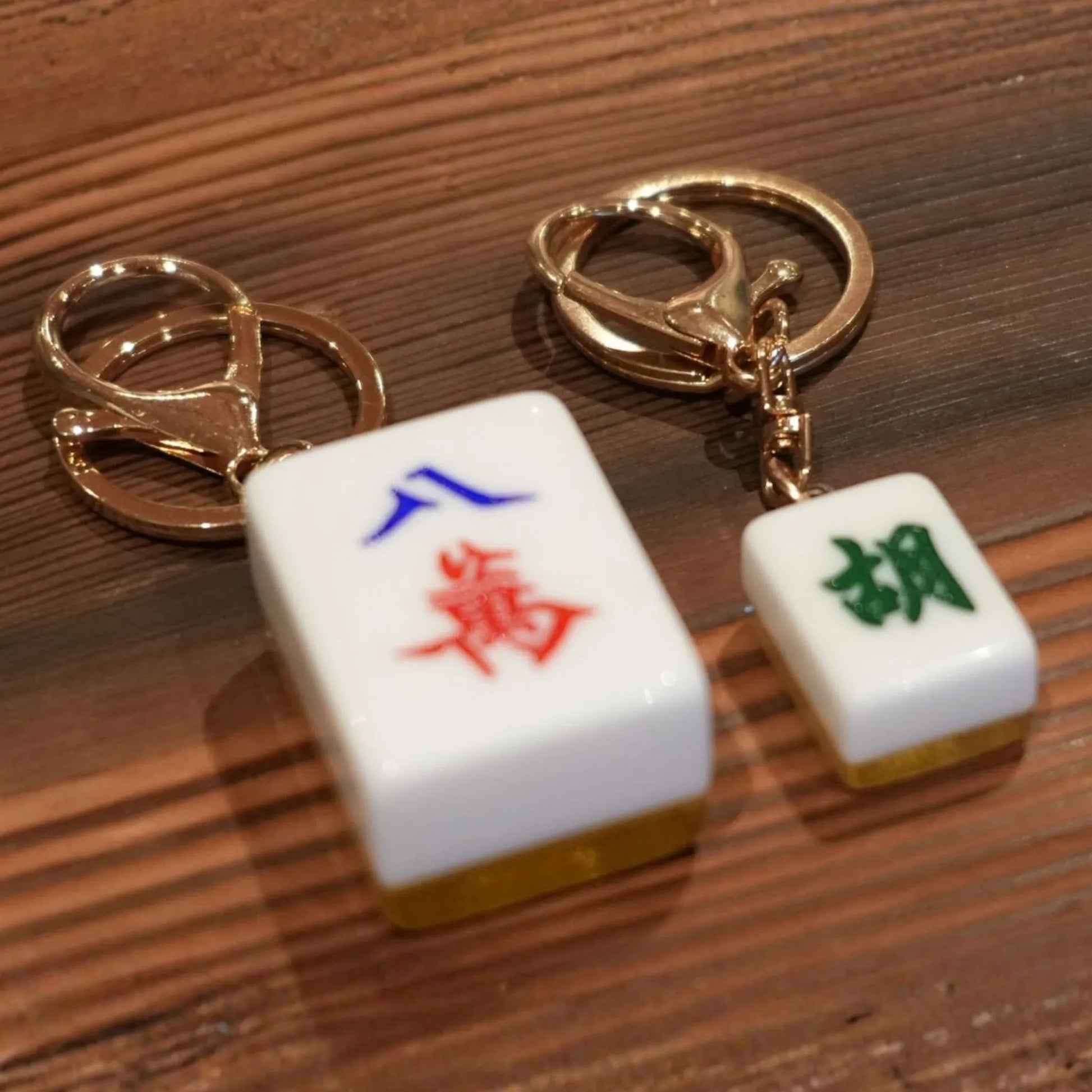 Two Mahjong-themed keychains on a wooden surface