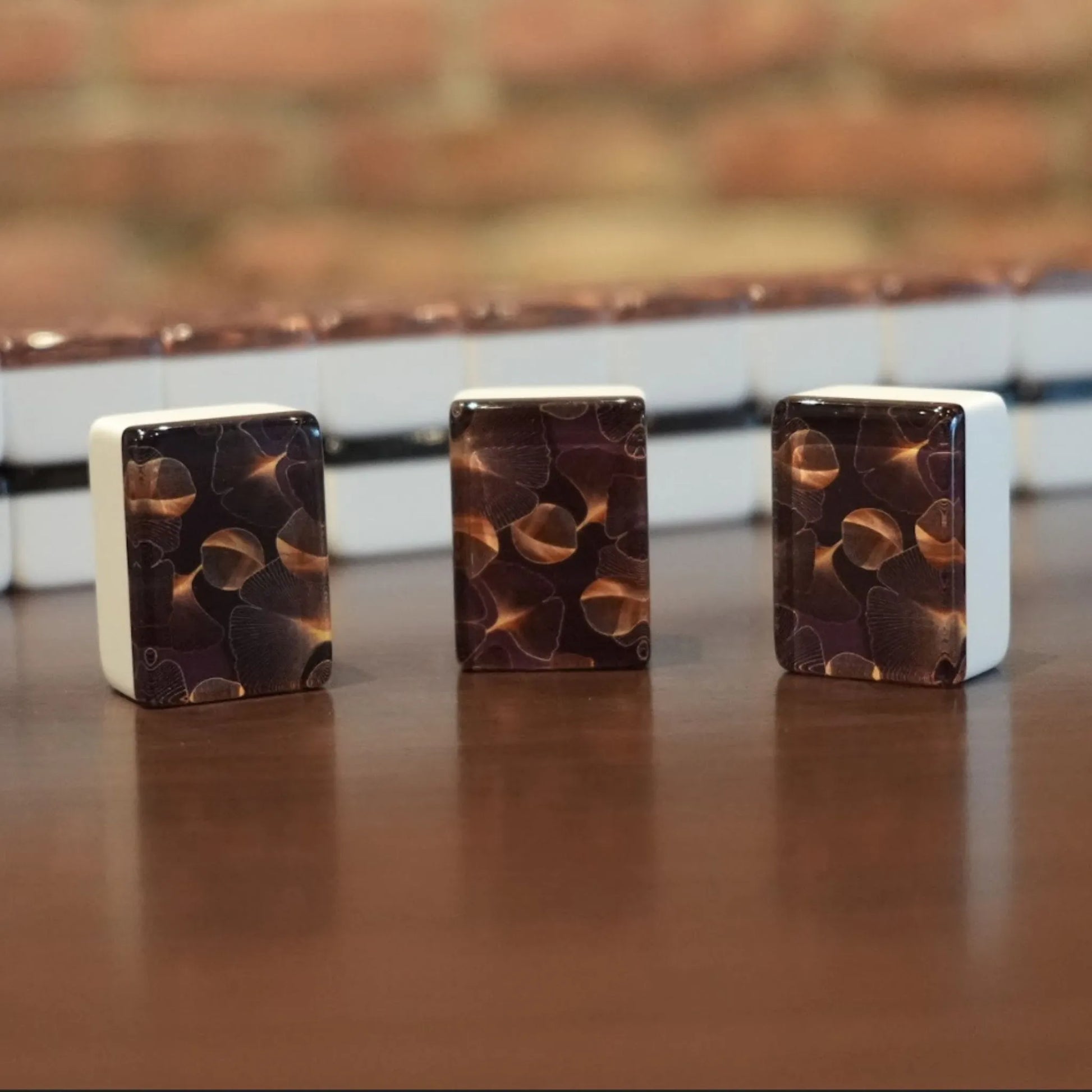Three standing gingo pattern mah jongg tiles displayed on a wooden table with a full wall of tiles in the background.