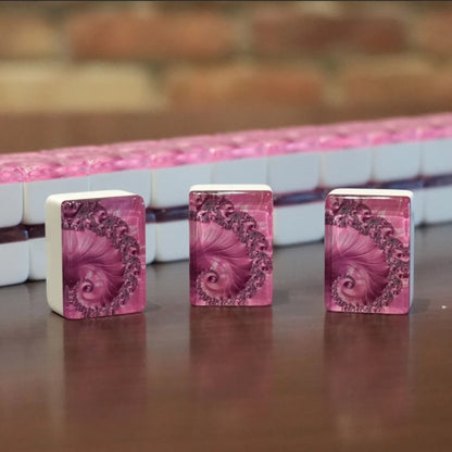 Three standing pink swirl mah jongg tiles displayed on a wooden table with a full wall of tiles in the background.