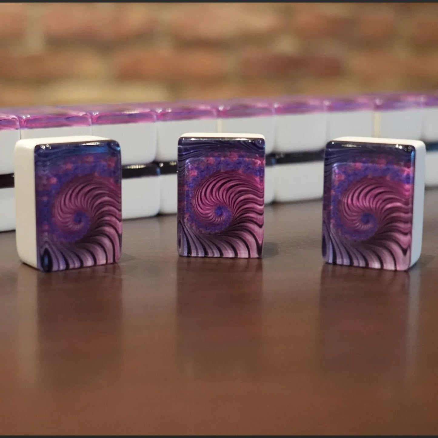 Three standing purple swirl mah jongg tiles displayed on a wooden table with a full wall of tiles in the background