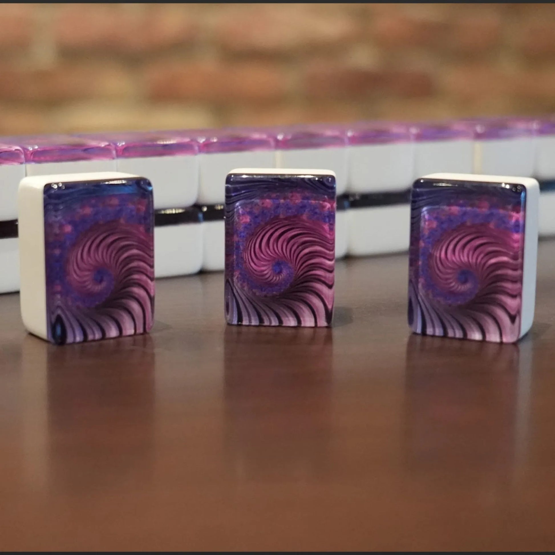 Three standing purple swirl mah jongg tiles displayed on a wooden table with a full wall of tiles in the background