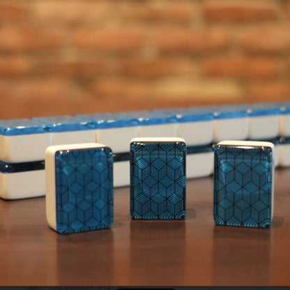 hree standing blue deco weave mah jongg tiles with a full wall of tiles in the background on a wooden table.